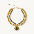 Double-strand champagne and olive pearl-effect pet necklace with a green floral pendant on a white surface.