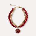 Double-strand red and champagne pearl-effect pet necklace with a red floral pendant on a white surface.
