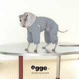 Dog wearing a gray check puffer bodysuit on a table.