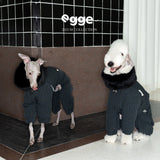 Two dogs wearing dark check puffer bodysuits with fluffy collars.