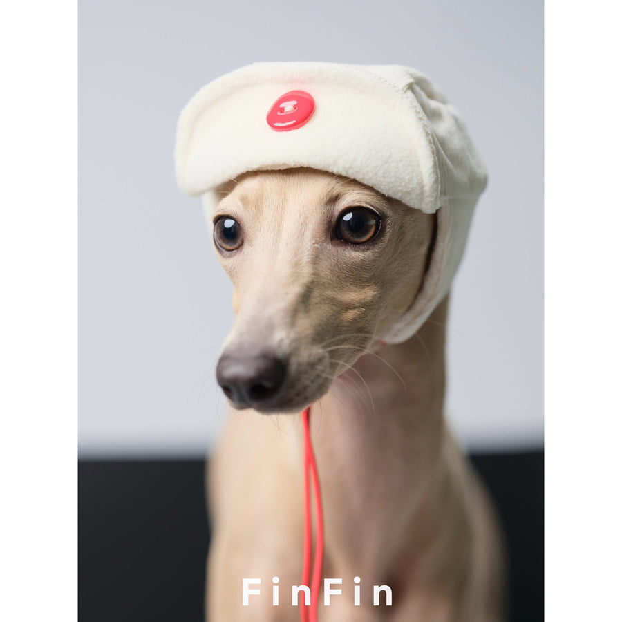 Close-up of a dog wearing a cream aviator hat with ear flaps.