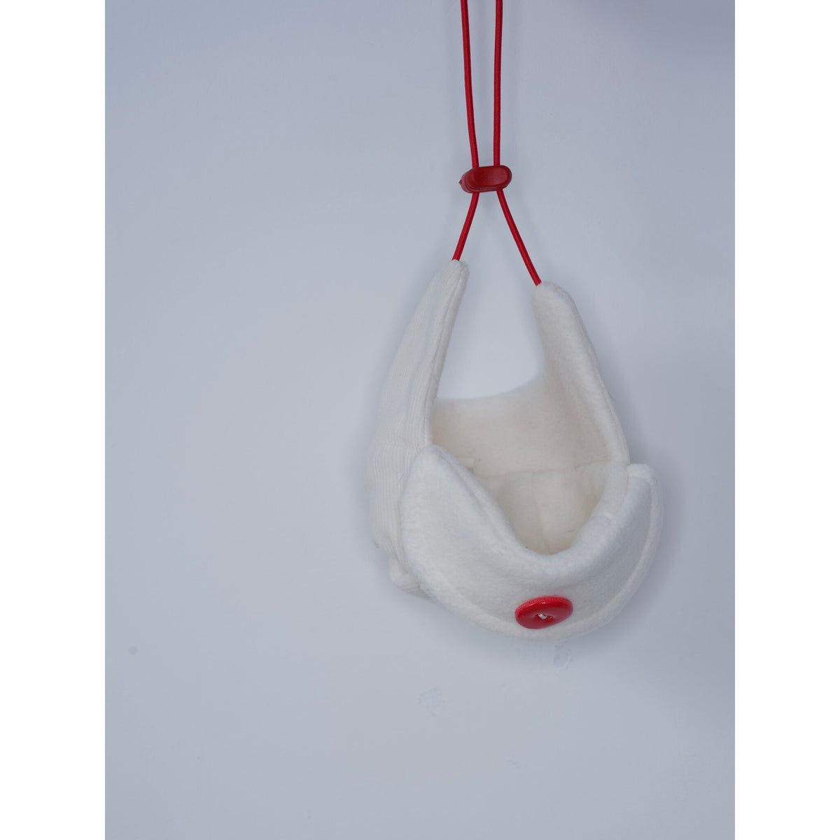 Cream dog aviator hat hanging from its red tie cords.