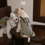 White dogs wearing pale green overalls with contrasting back straps.
