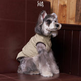 Schnauzer wearing a cream padded vest with brown trim.